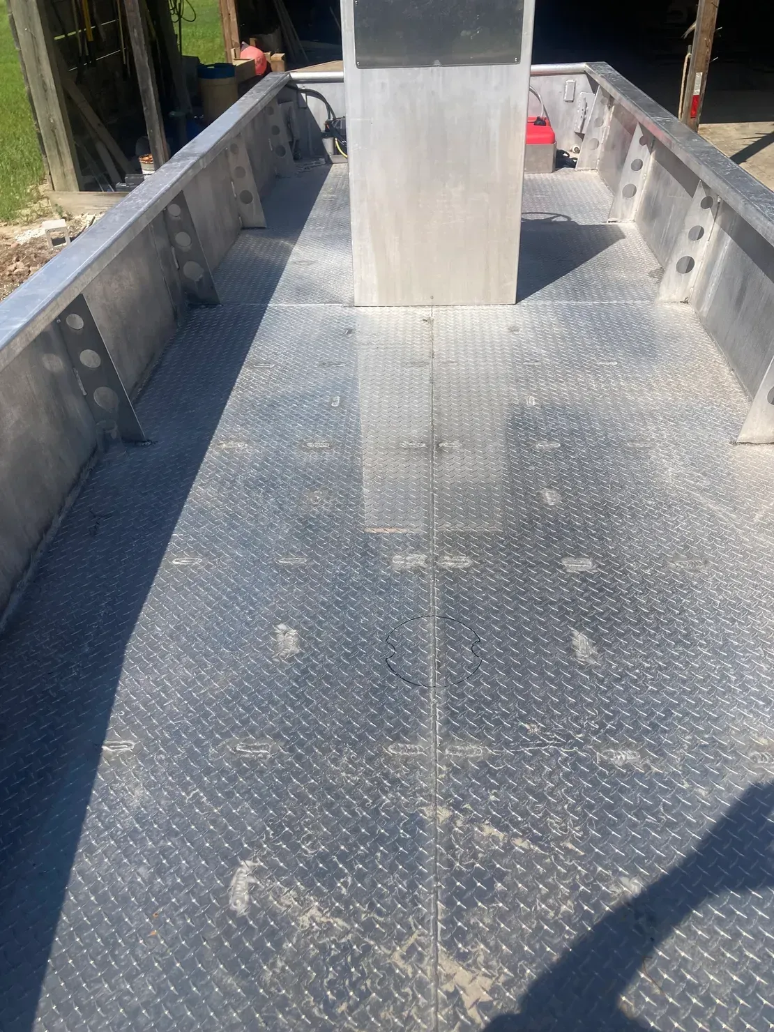 Interior view of an aluminum boat deck featuring diamond-plate flooring and a central steering console.