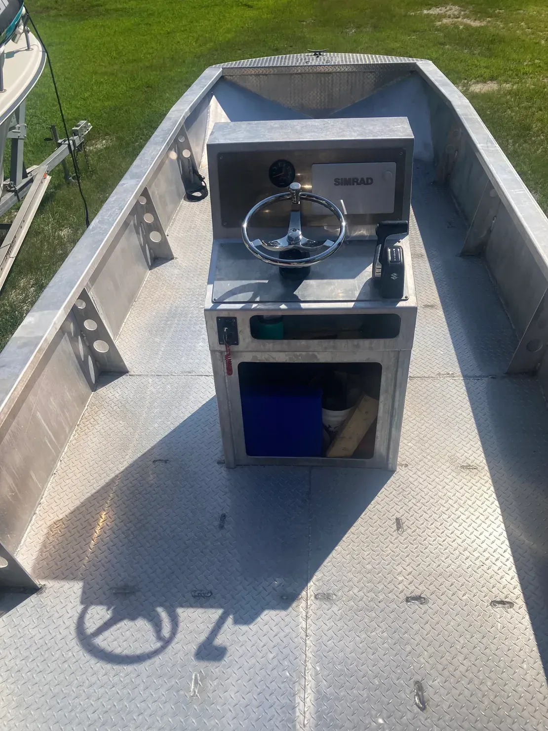 Interior view of an aluminum flat-bottom boat showing a center console with a steering wheel and a checkered floor plate.