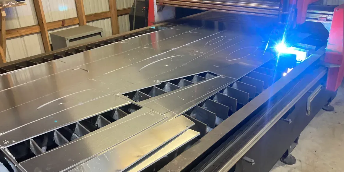 A CNC laser cutter machine slices a large metal sheet in an industrial workshop.