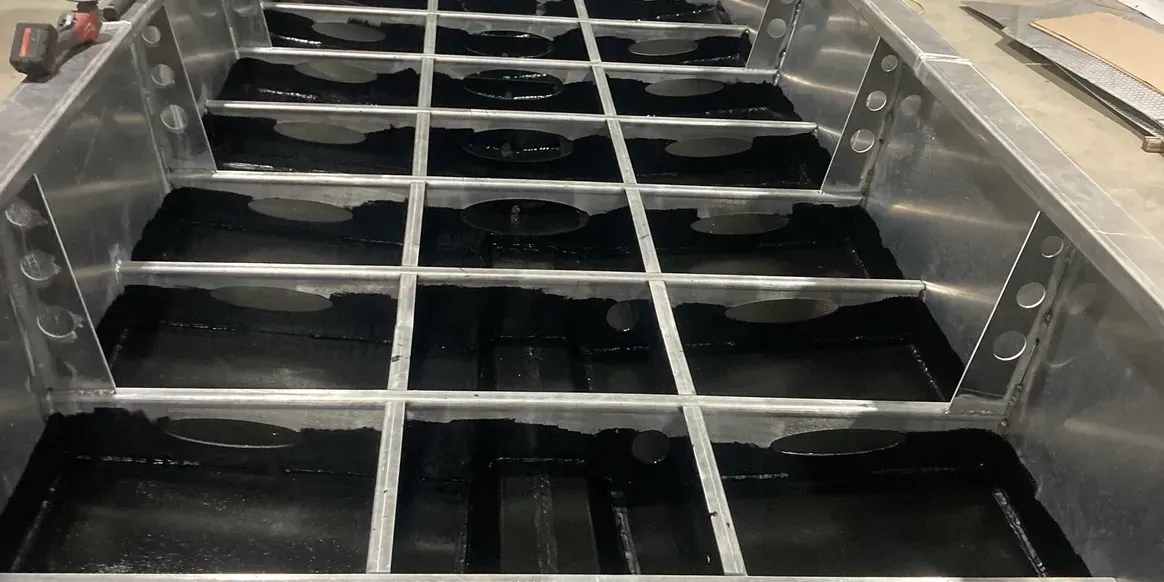 A metal framework with a grid of beams installed over a black surface inside an unfinished boat hull.