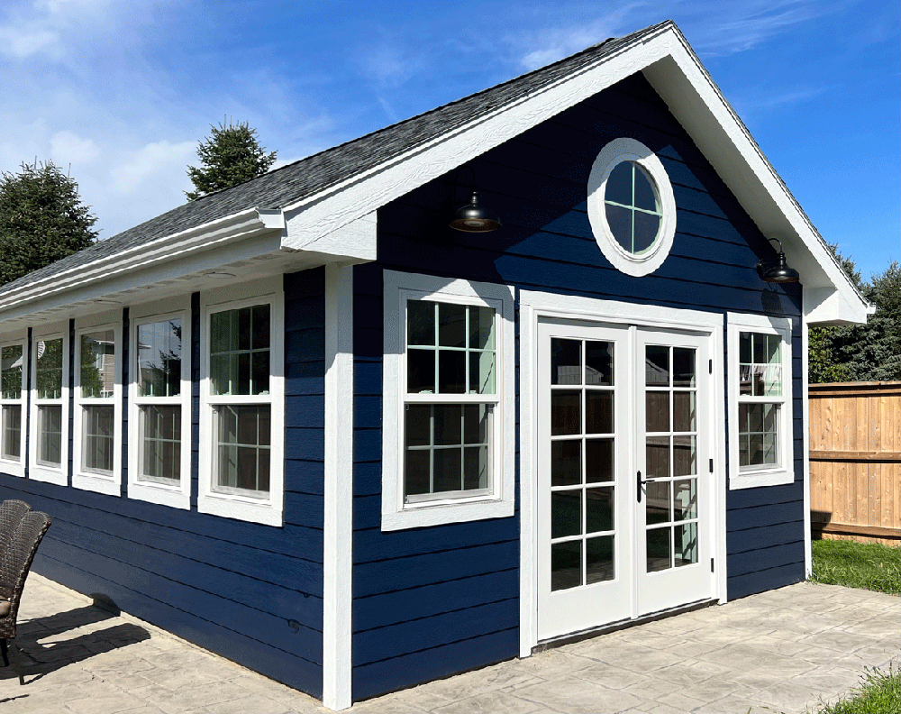 Blue shed with white trim, double doors, and oval window, under a clear sky.