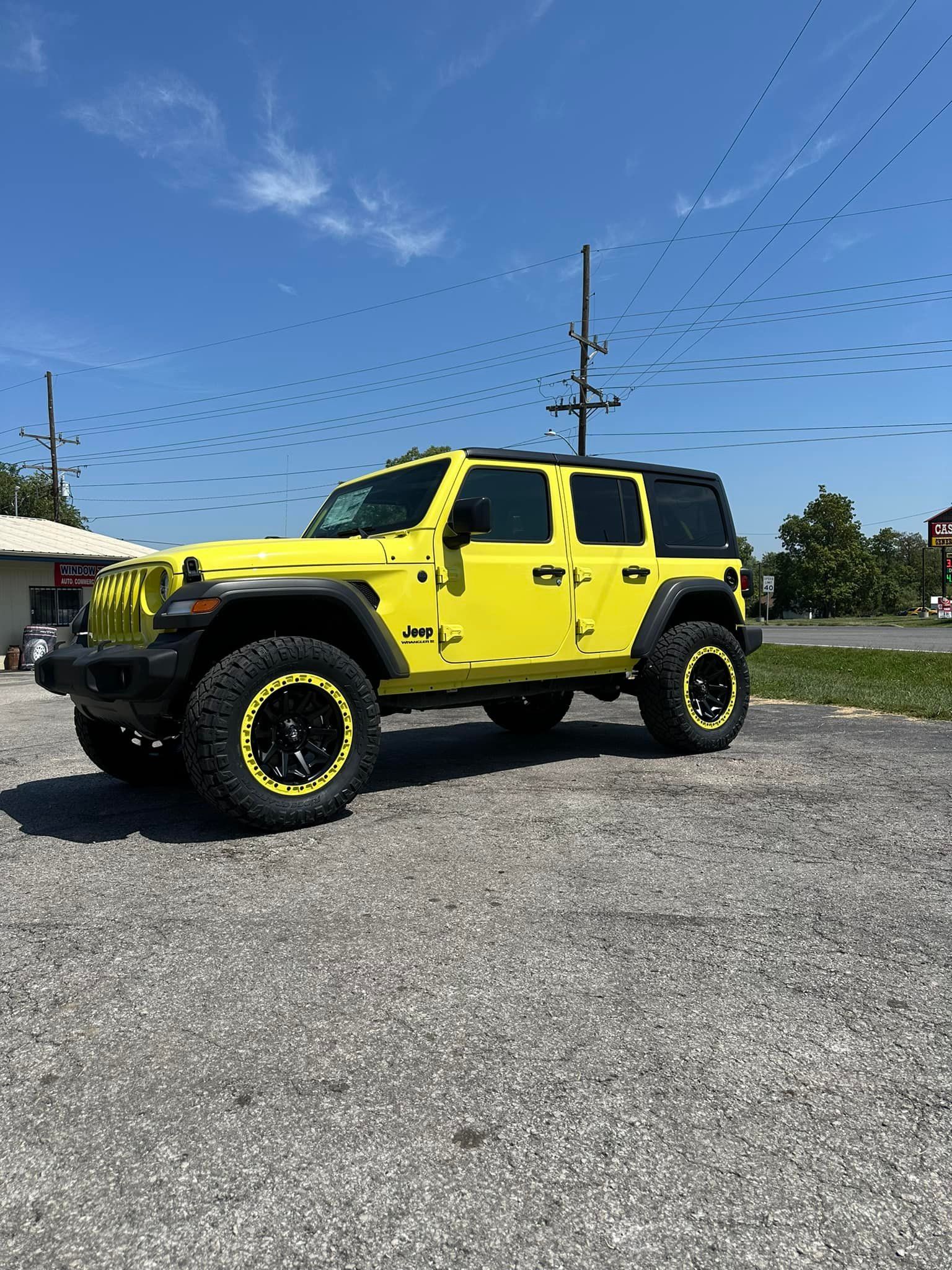 A yellow jeep wrangler is parked in a gravel lot.
