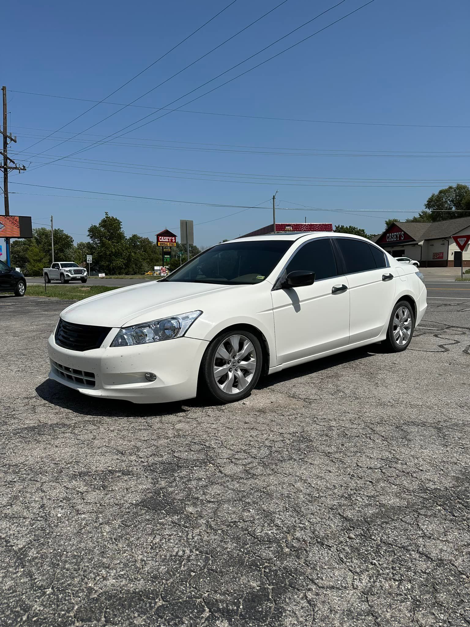 A white honda accord is parked in a gravel lot.