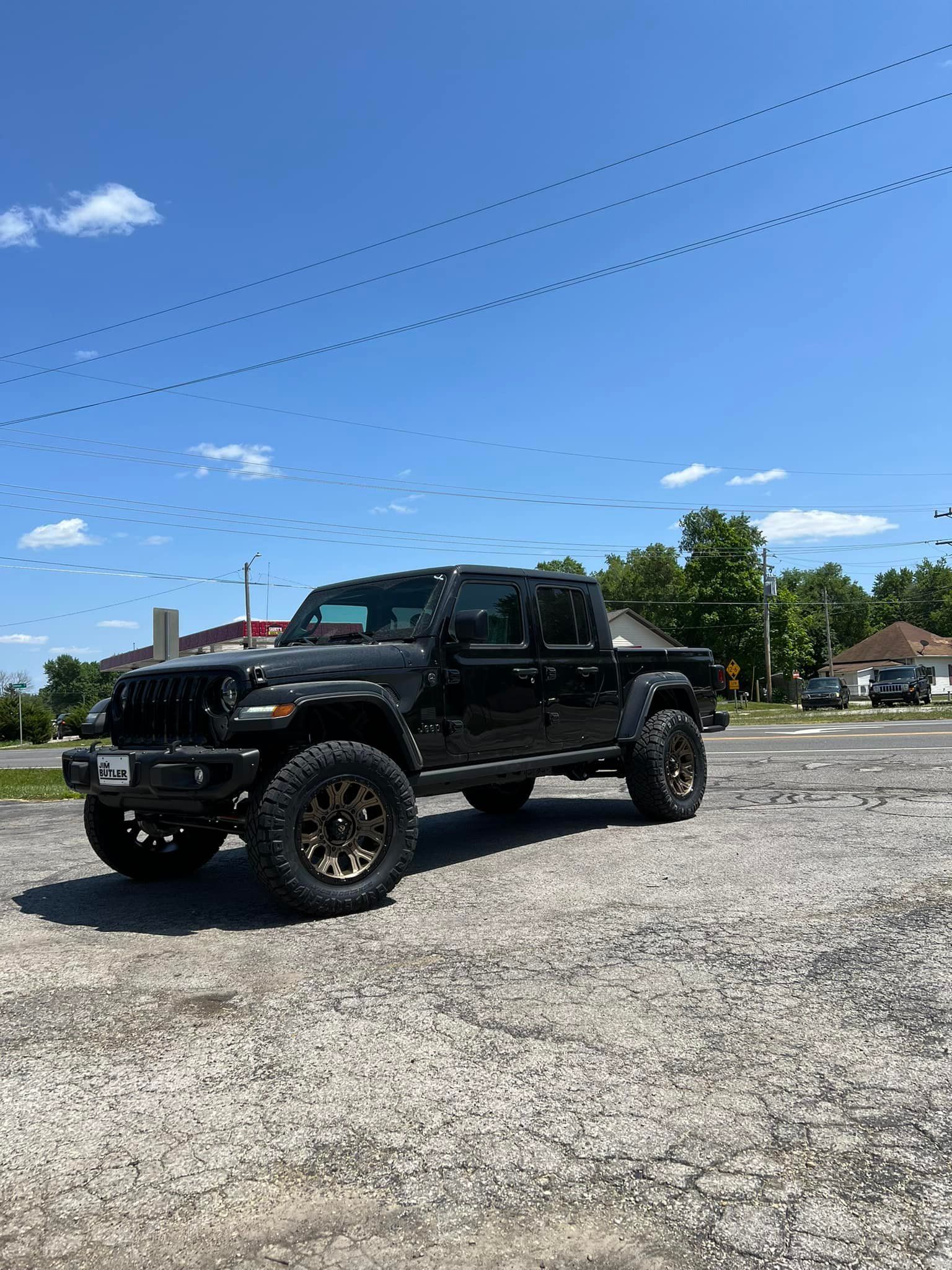 A black jeep is parked in a gravel lot.