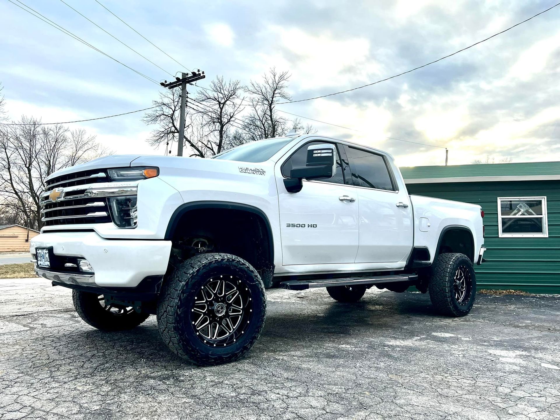 A white truck is parked in front of a green building.