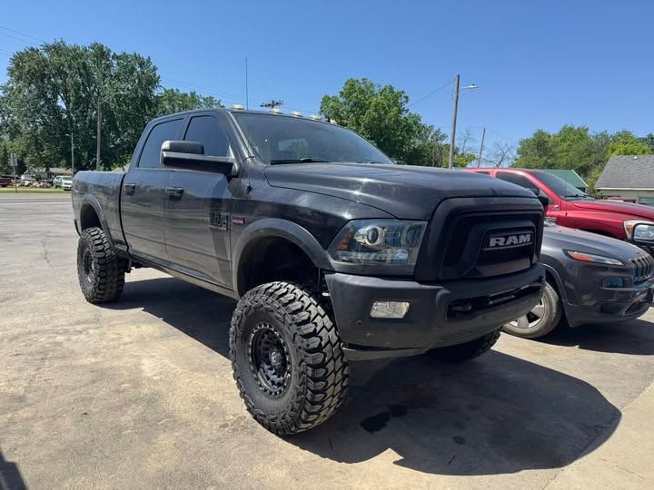 A black ram truck is parked next to a red truck in a parking lot.