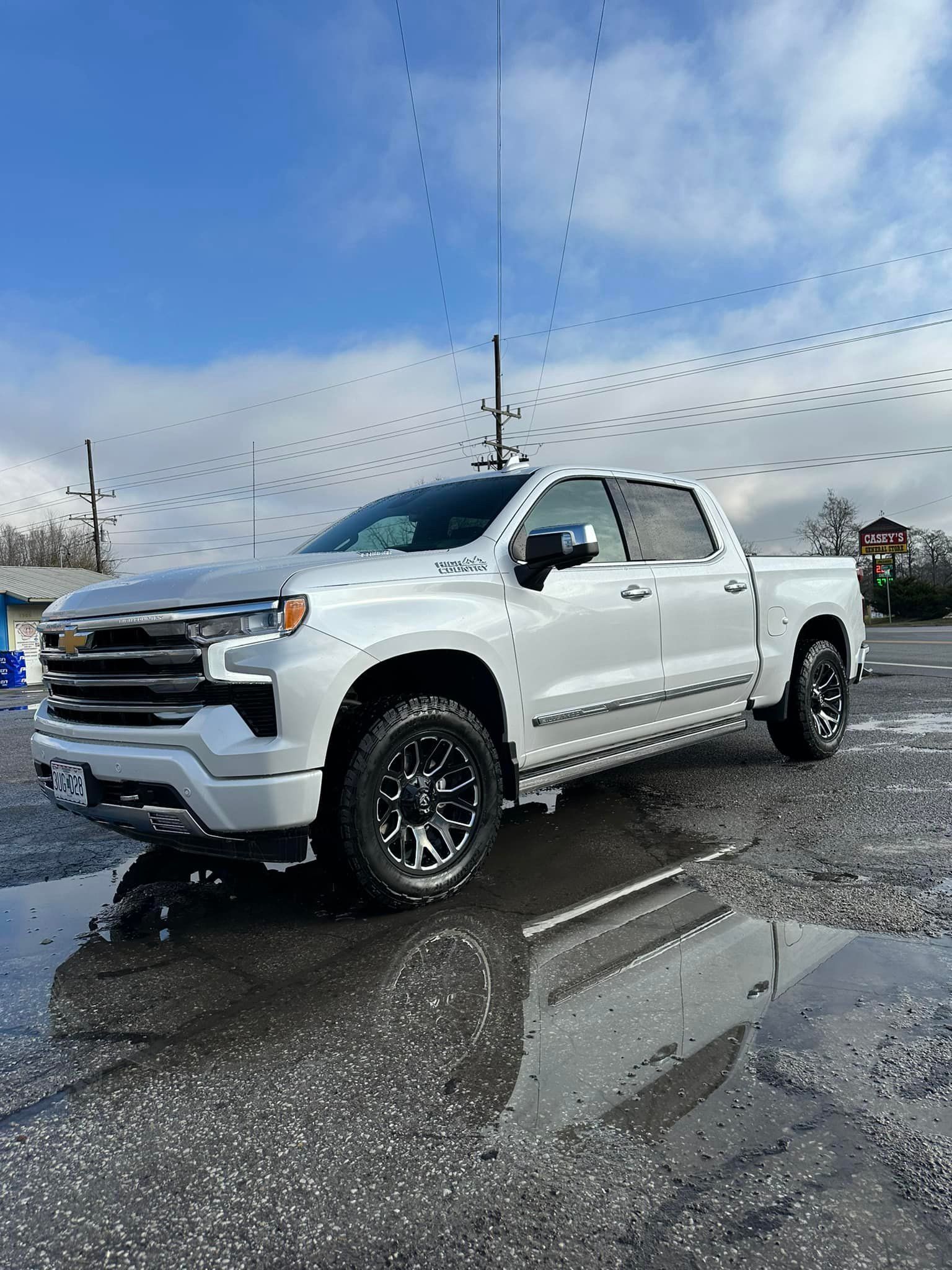 A white truck is parked in a puddle of water in a parking lot.