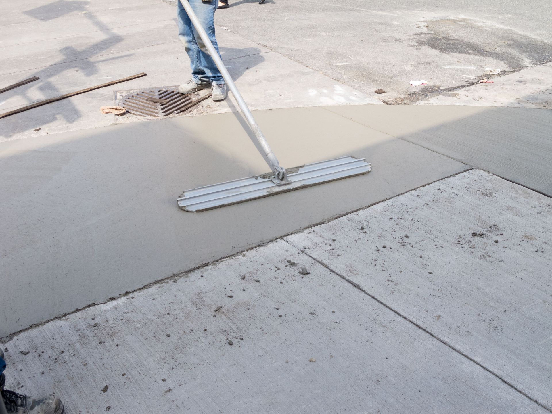 Person using a concrete float to smooth wet concrete on a sidewalk.