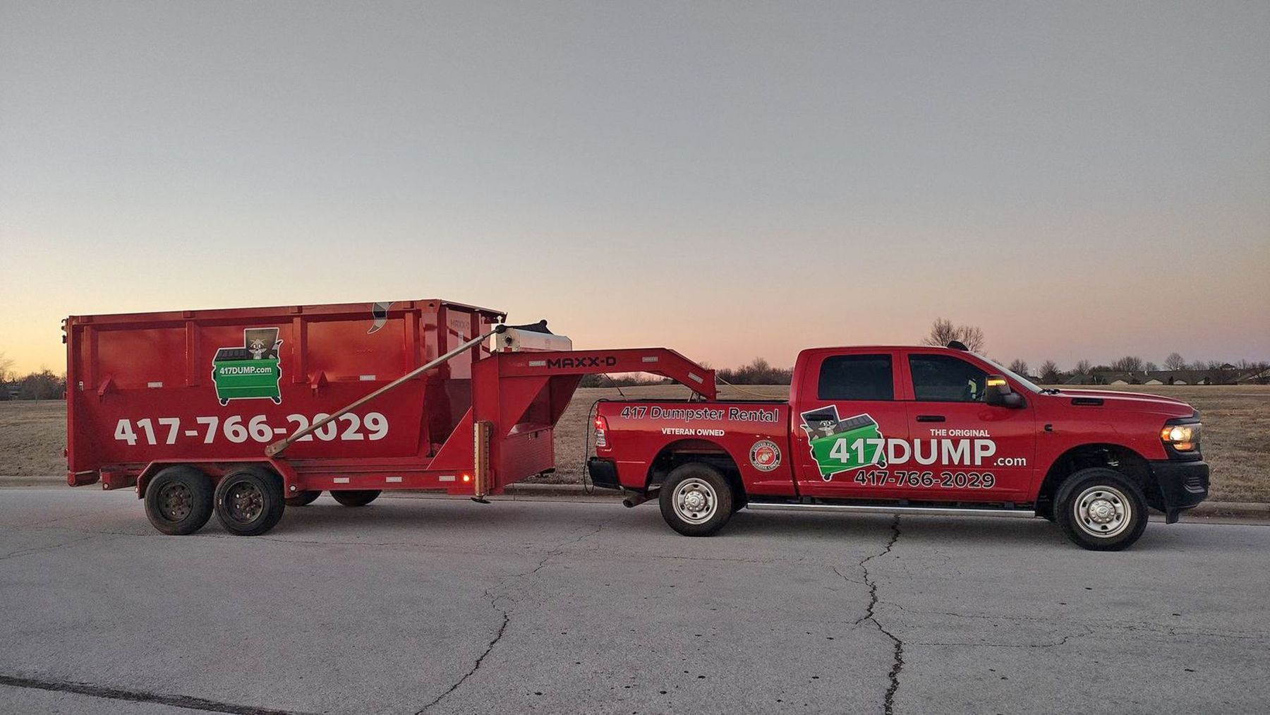 A red dump truck with a trailer attached to it is parked on the side of the road.