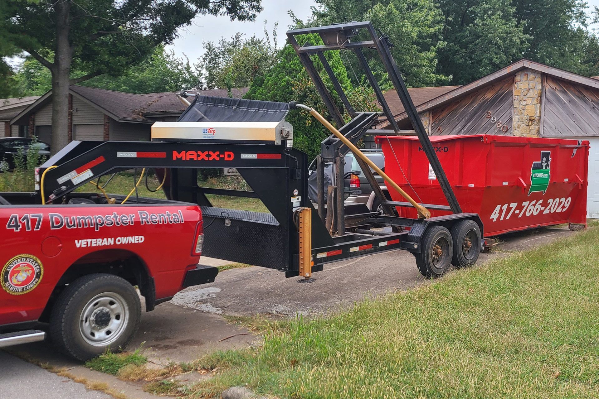 A red truck is towing a dumpster on a trailer.