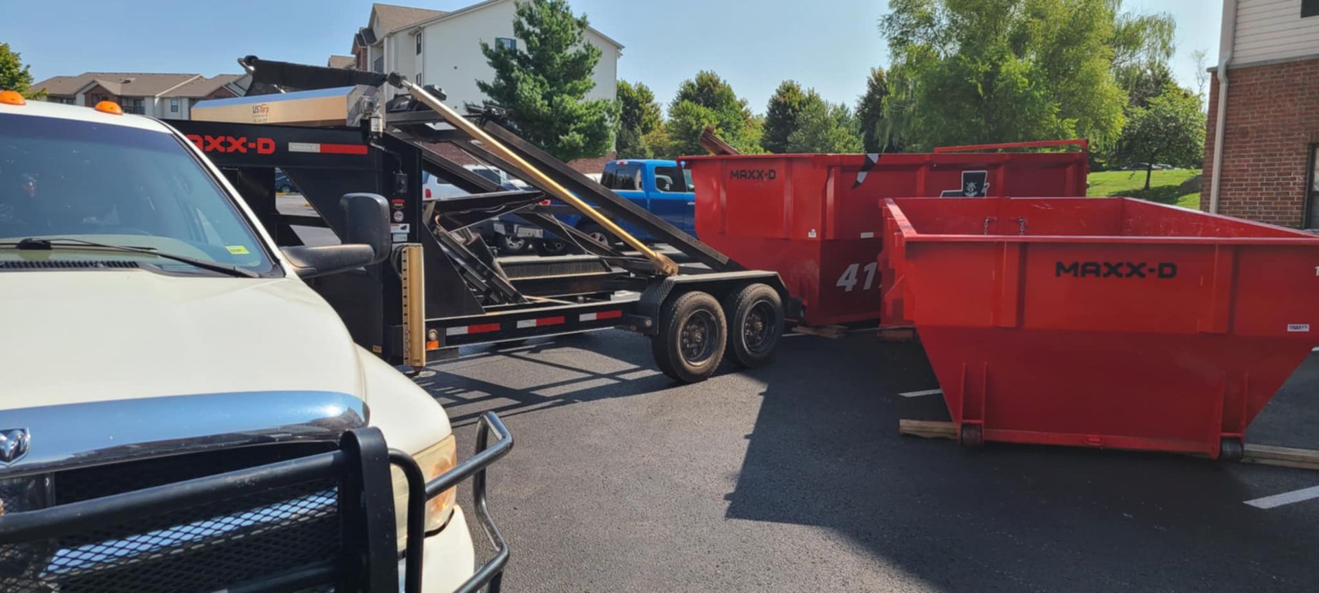A dumpster is being loaded onto a trailer next to a truck.