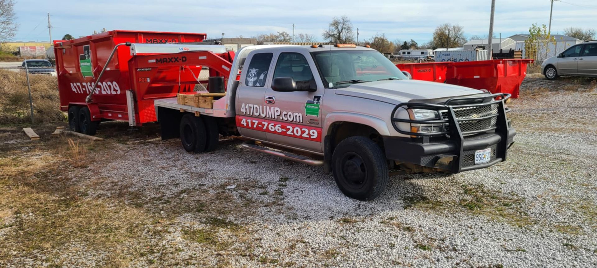 A truck with a trailer attached to it is parked in a gravel lot.
