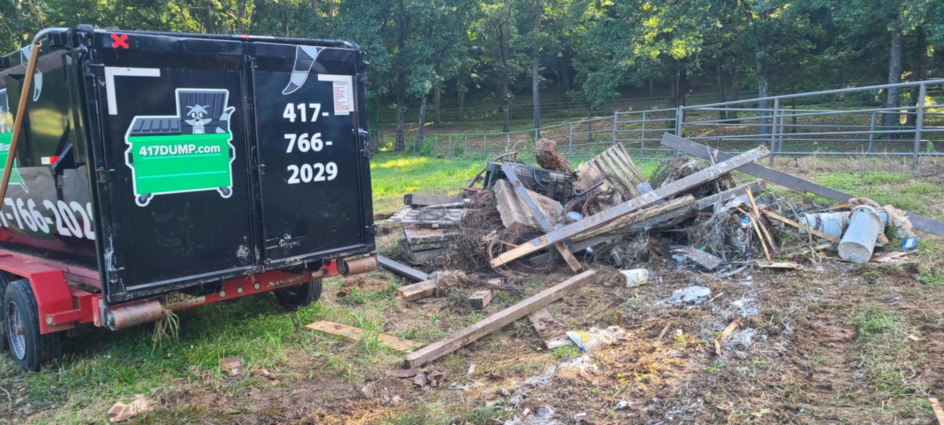 A black truck is parked in a field next to a pile of wood.