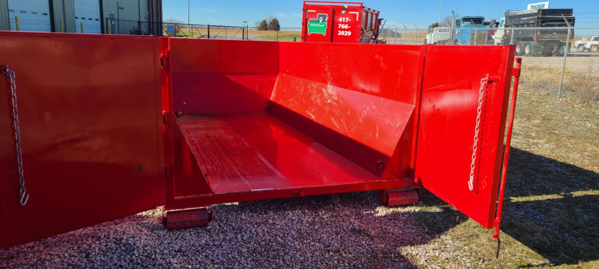 A red dumpster is sitting on top of a gravel field.