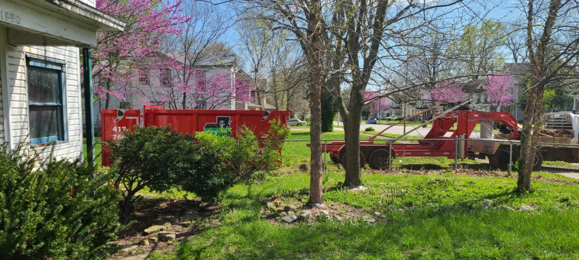 A red dumpster is parked in the grass in front of a house.