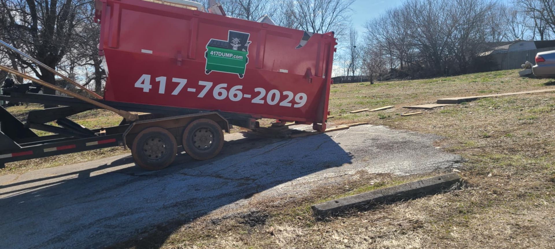 A red dumpster is sitting on top of a trailer in a field.