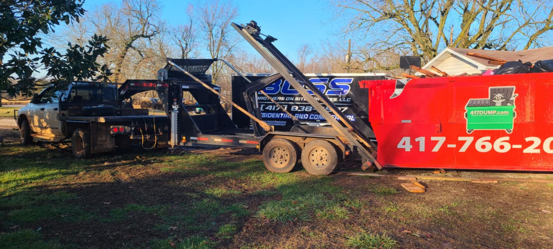 A dumpster is sitting on top of a trailer next to a truck.
