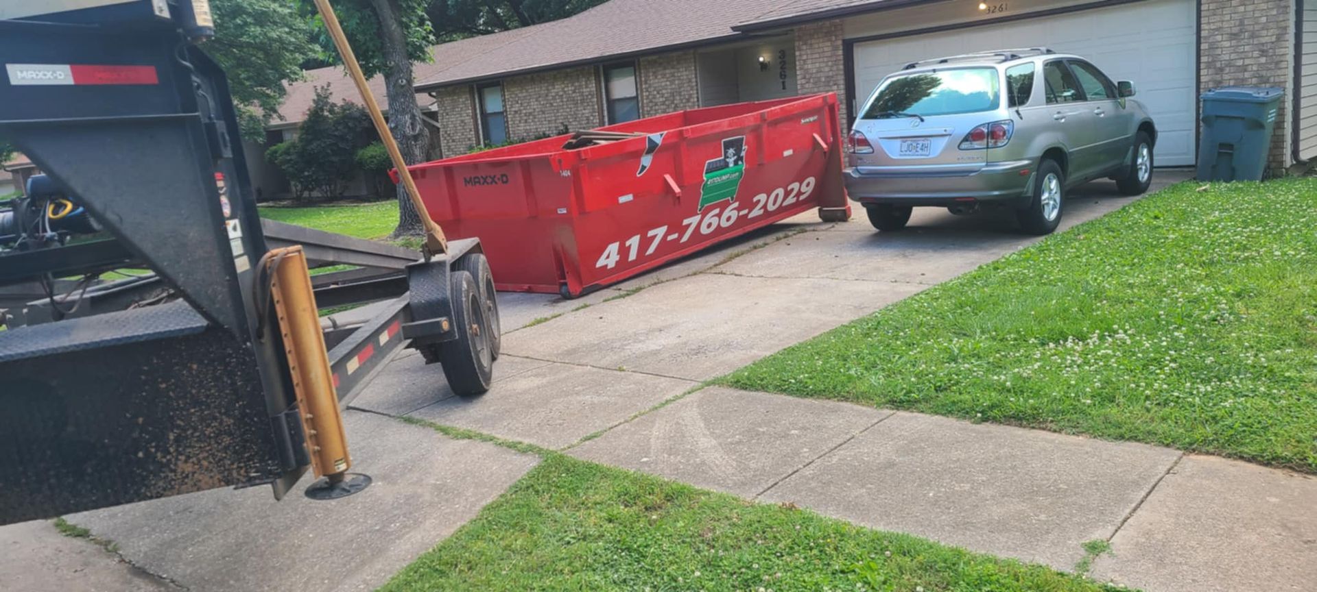 A dumpster on a trailer is parked in front of a house.