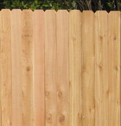 A close-up of a natural light-brown wooden picket fence with pointed tops.