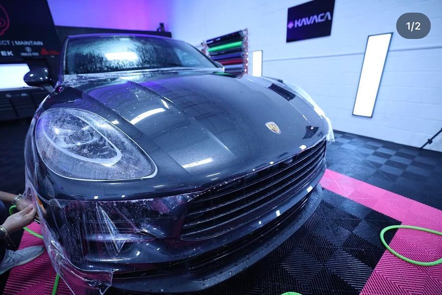 Dark gray Porsche with protective film being applied in a detailing shop.