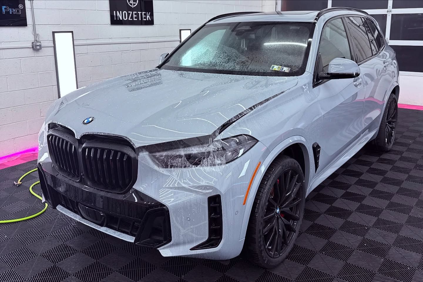 Light blue BMW X5 SUV with black accents parked inside a detailing shop.