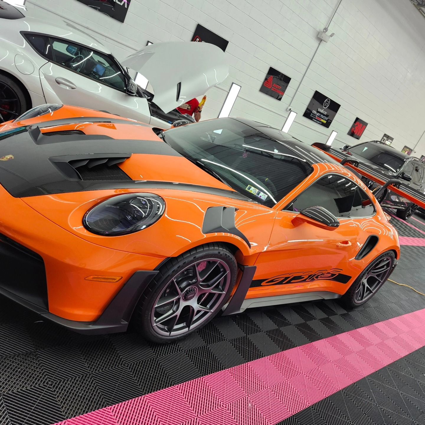 Orange Porsche 911 GT3 RS with black accents in a car detailing shop.