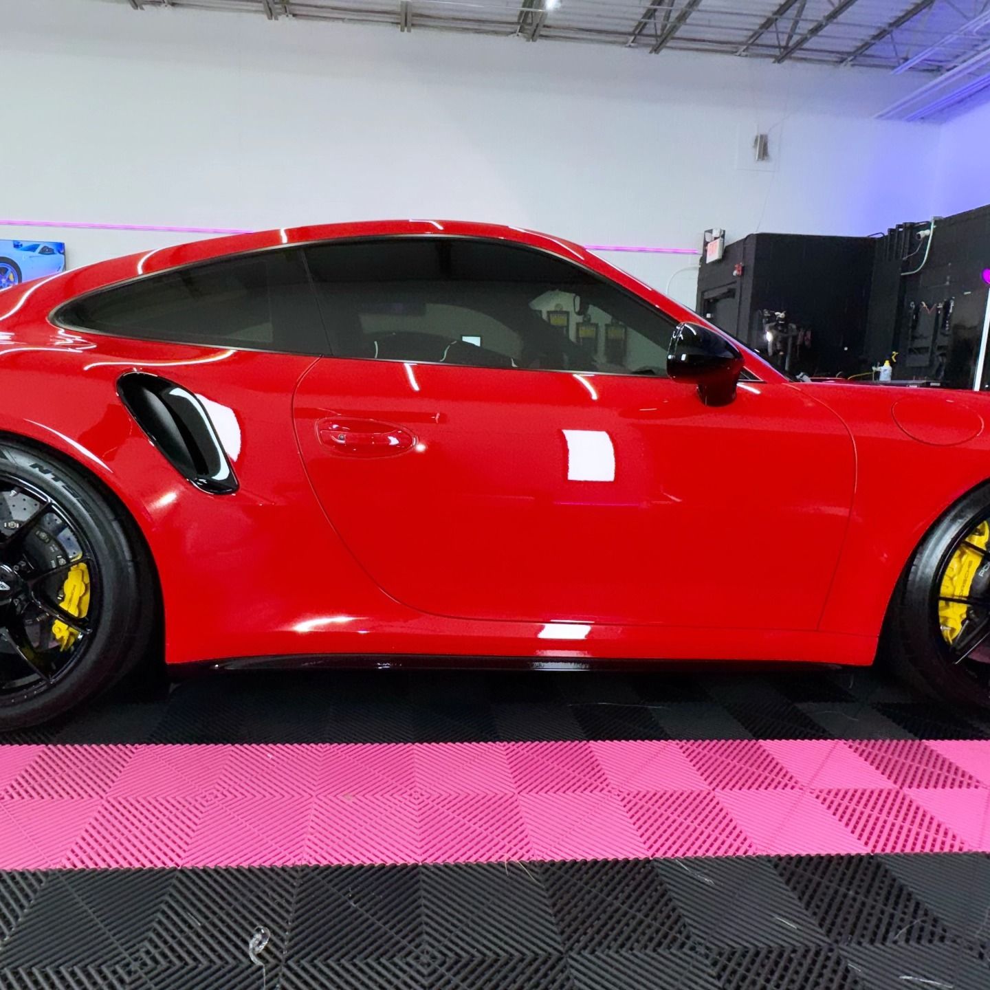 Red sports car with black wheels and yellow brake calipers parked on a checkered floor.