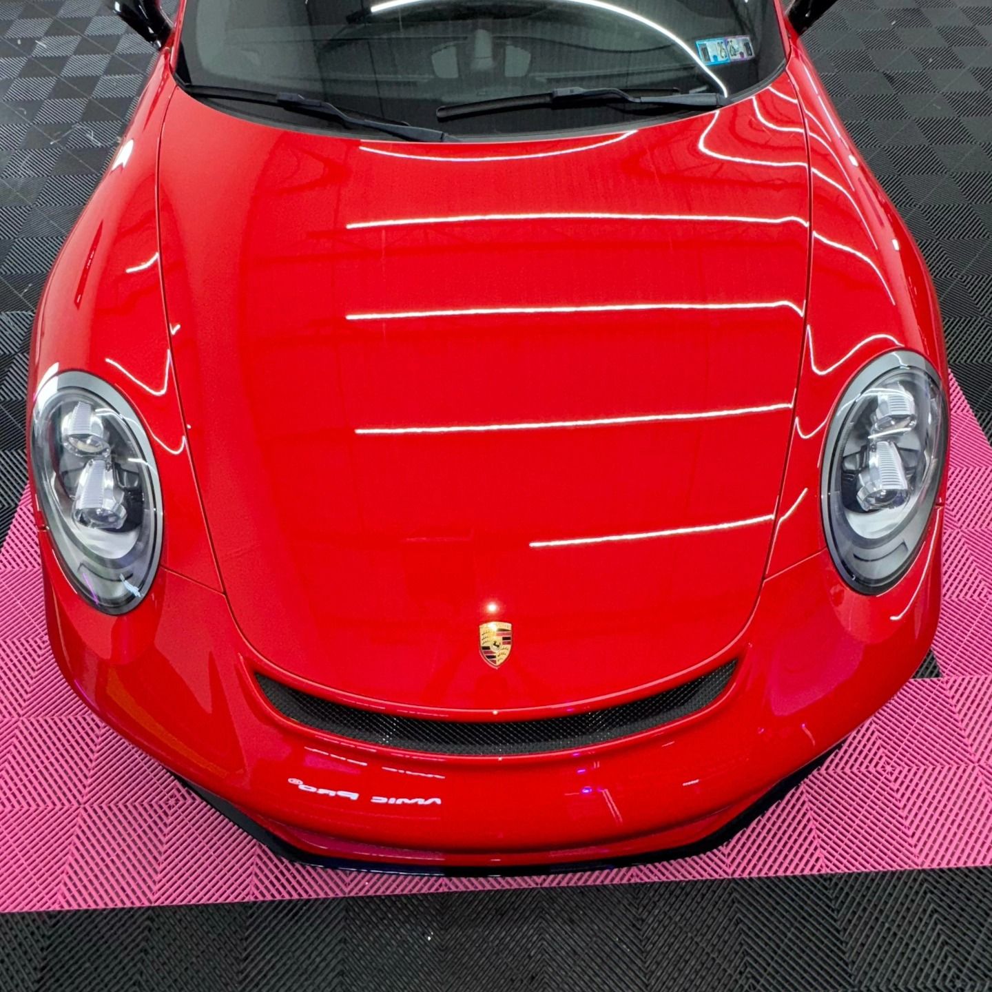 Red Porsche car, front view, on a pink floor with multiple bright white lines reflecting off the hood.