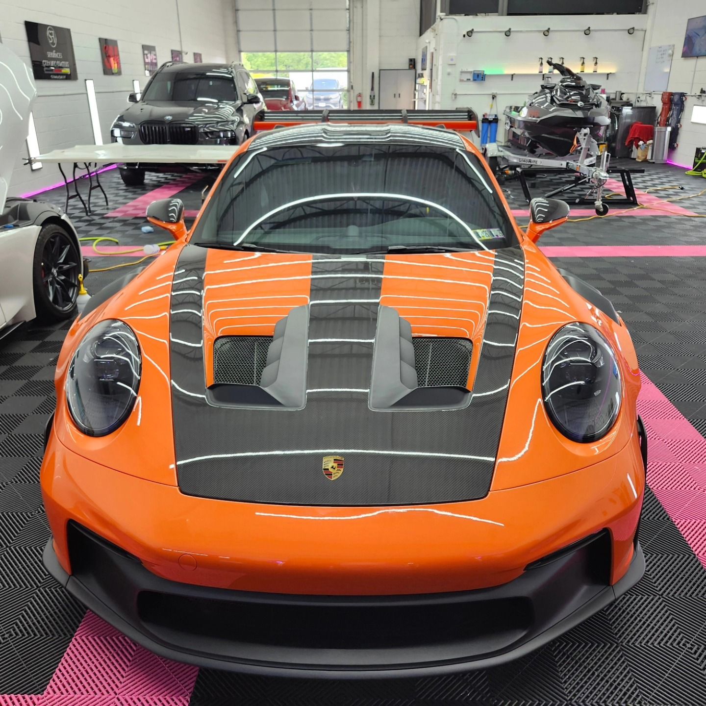 Bright orange Porsche sports car with black hood in a detailing shop.