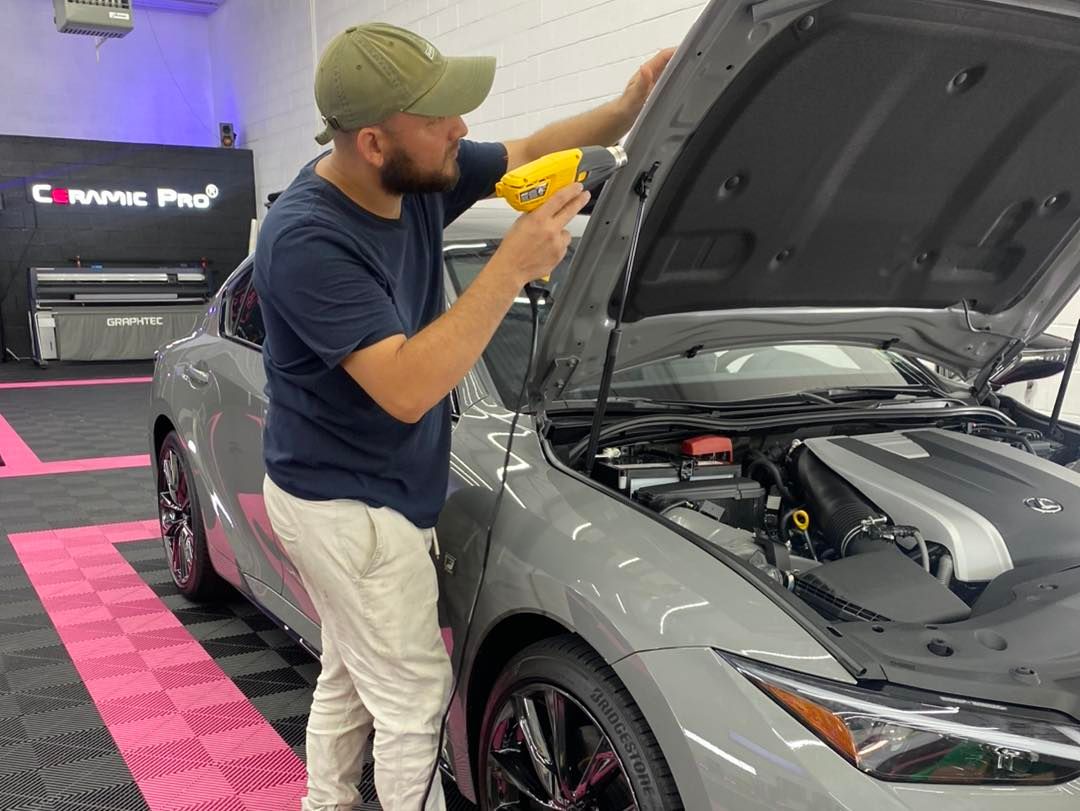 Man using heat gun on gray car hood. Garage setting.