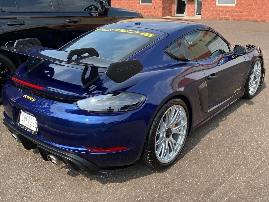 Blue Porsche sports car parked outside on a sunny day, with large rear spoiler and silver wheels.