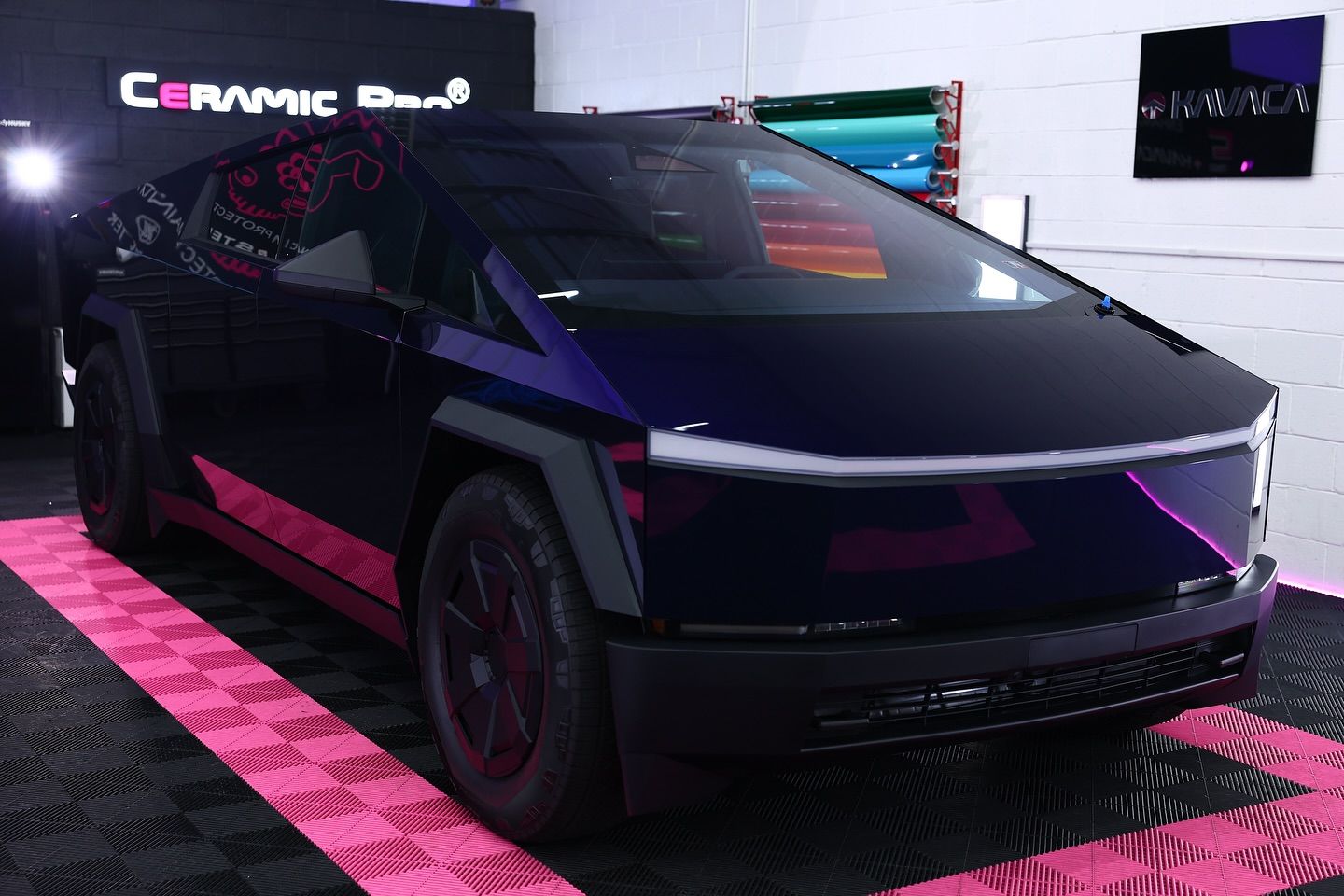 Tesla Cybertruck with purple accents on a pink checkered floor at an auto show.