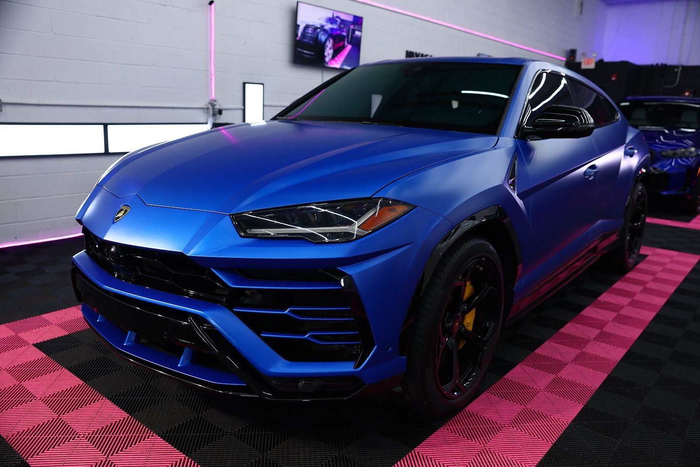 Blue Lamborghini SUV parked in a garage with pink and black accents.