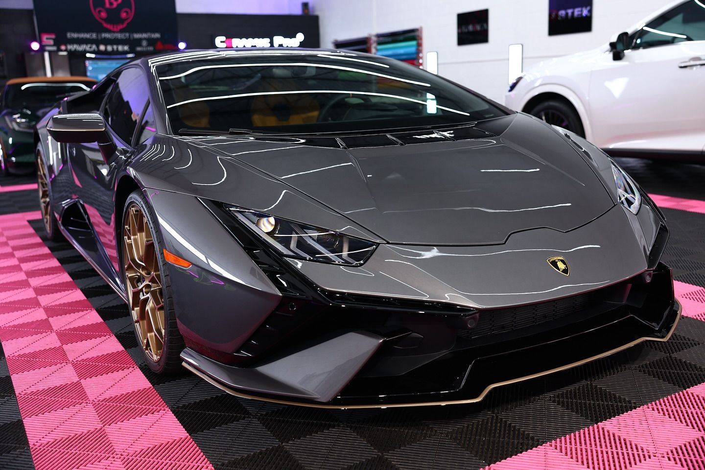 Gray Lamborghini sports car with gold wheels and trim, indoors on a pink and black floor.
