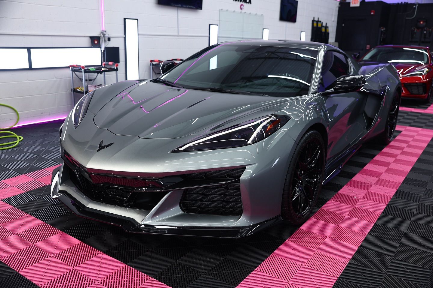 Silver Corvette sports car parked in a detail shop with pink and black flooring.