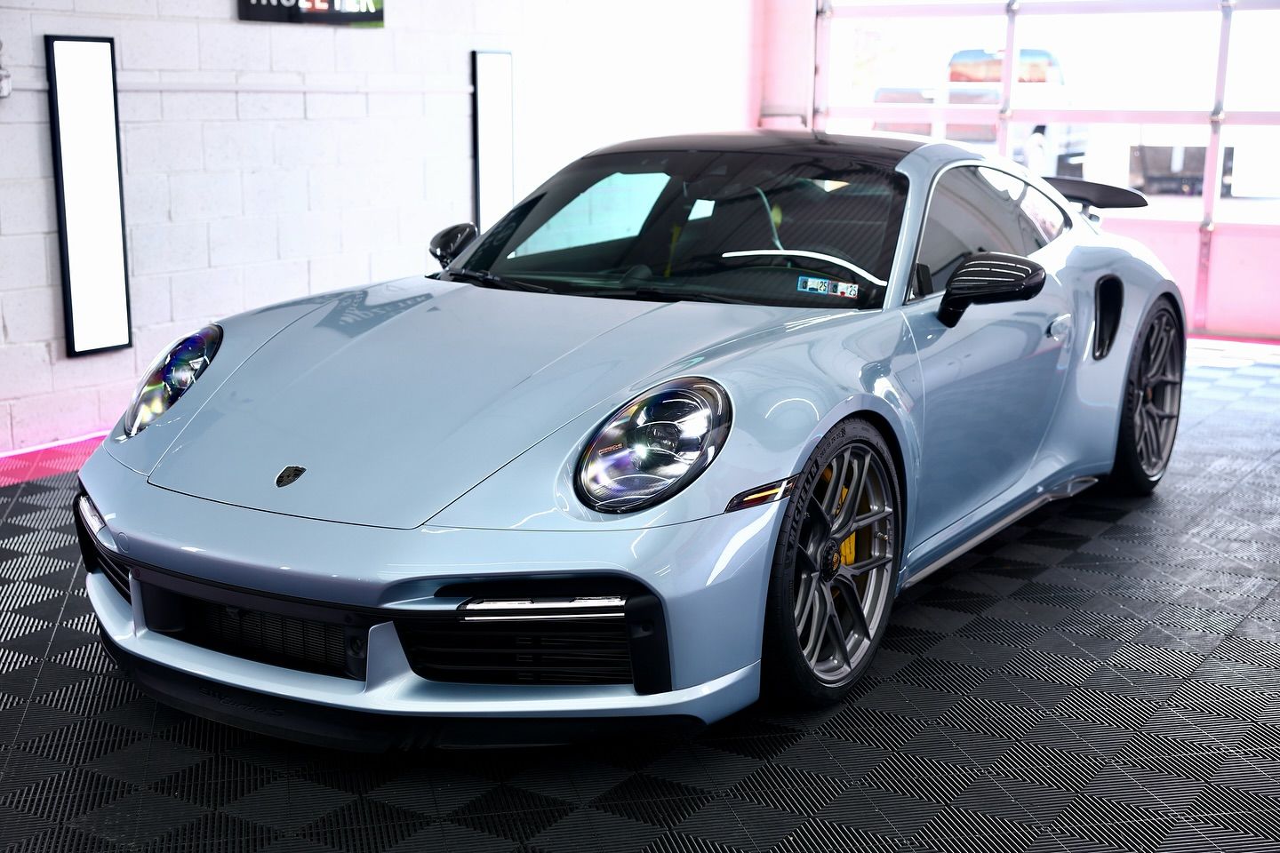 Light blue Porsche 911 Turbo S sports car, black roof, parked inside a well-lit garage.
