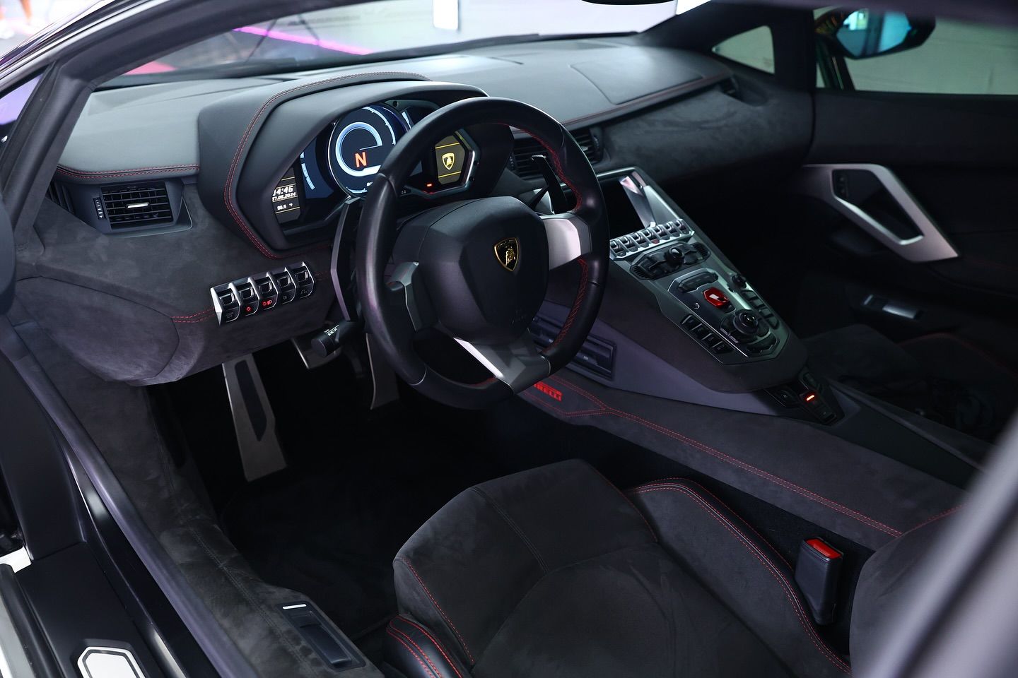 Black Lamborghini interior with red stitching, steering wheel, dashboard, and console.