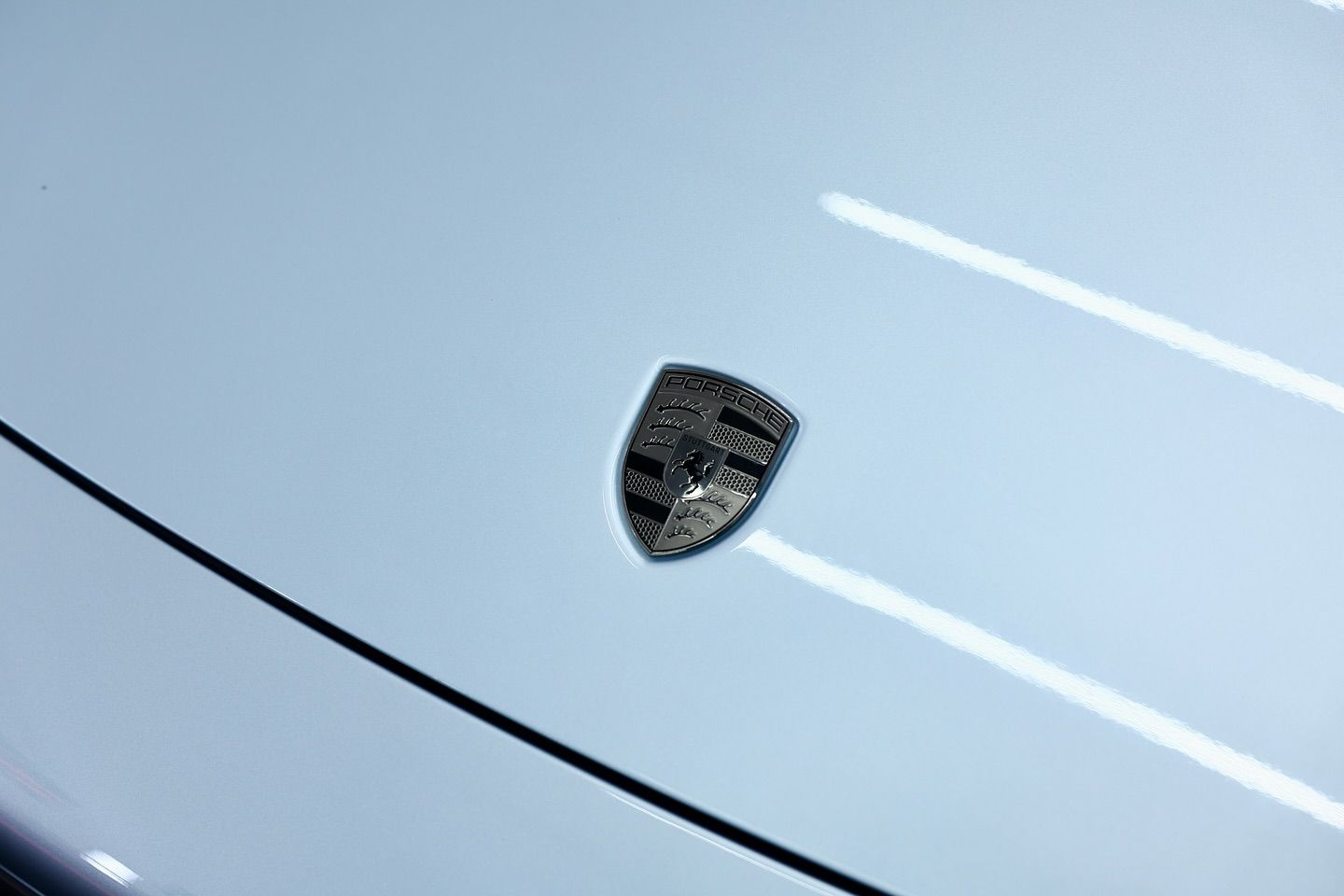 Silver Porsche emblem on light blue car hood.