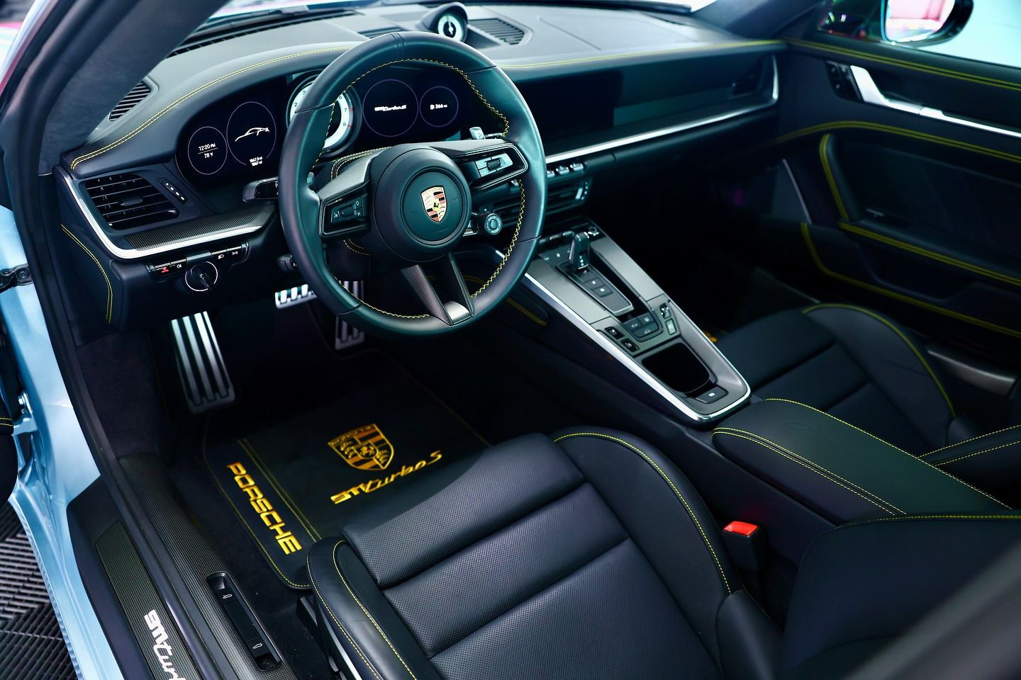 Interior of a Porsche 911 Turbo S with black leather seats, yellow stitching, and a black and gold floor mat.