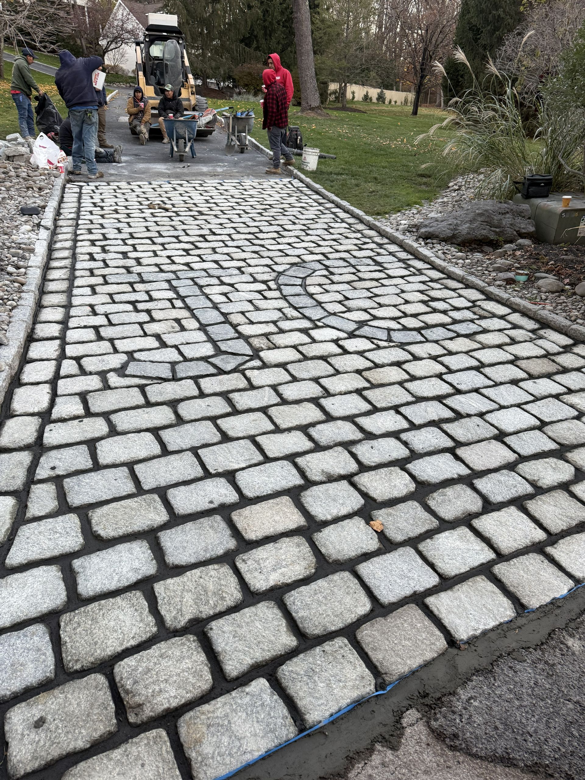 Workers are installing granite cobblestone pavers for a driveway.