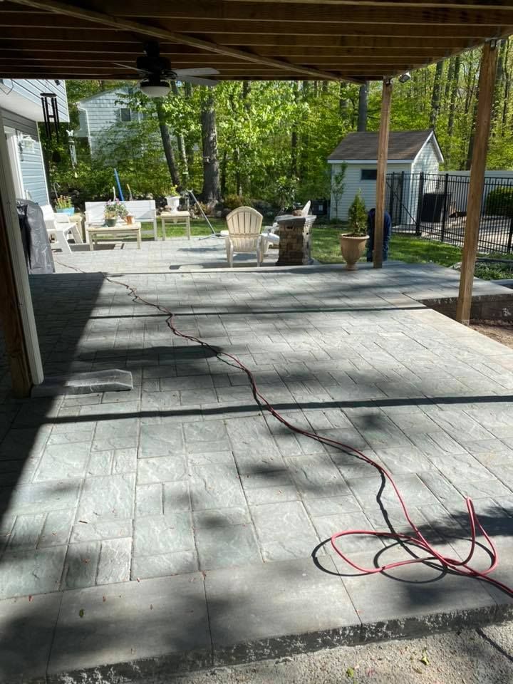 Gray paver patio with red cord, outdoor seating, trees in the background, under a wooden pergola.