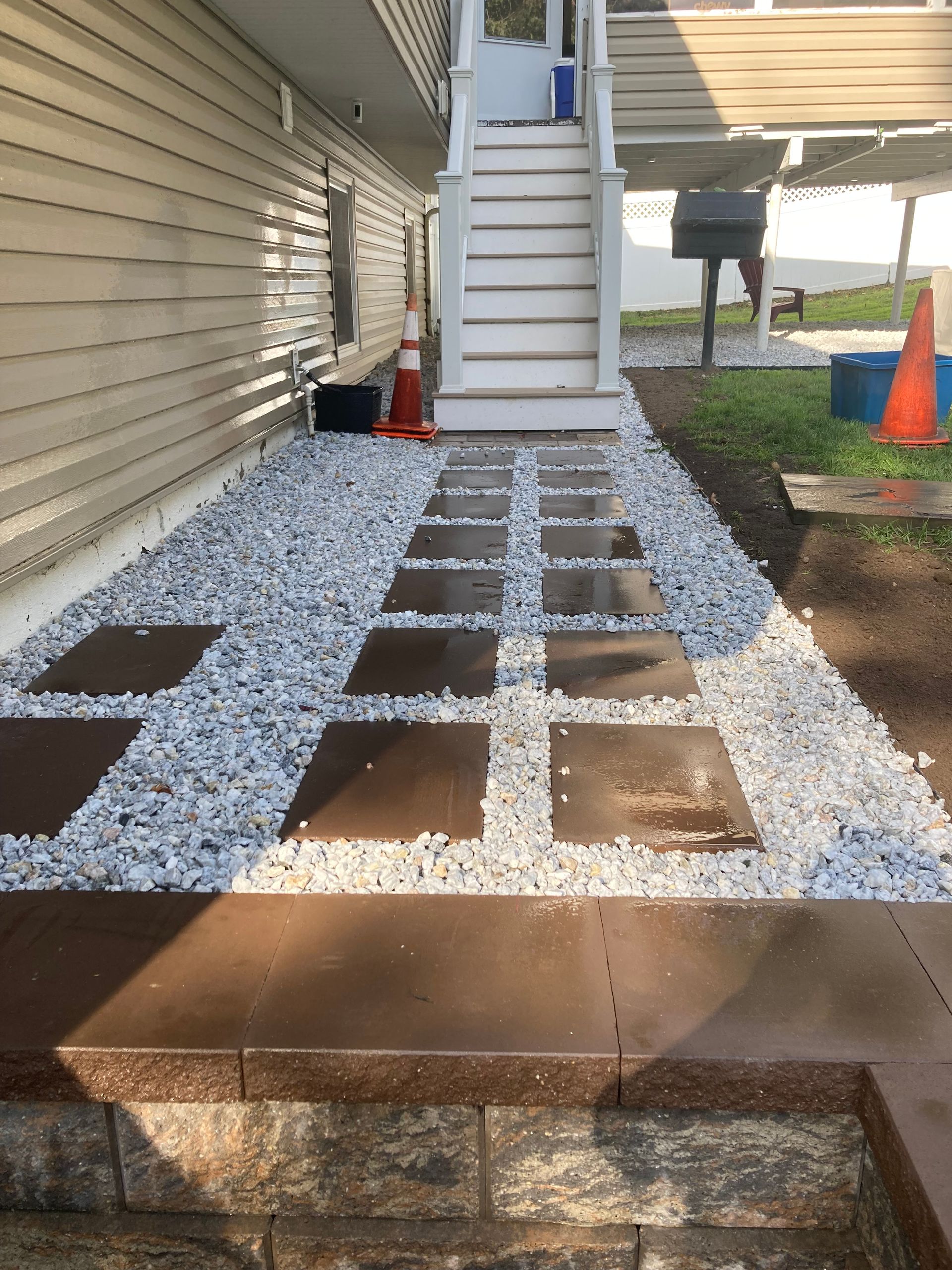 Pathway of square stepping stones surrounded by white gravel, leading to stairs, next to a building.