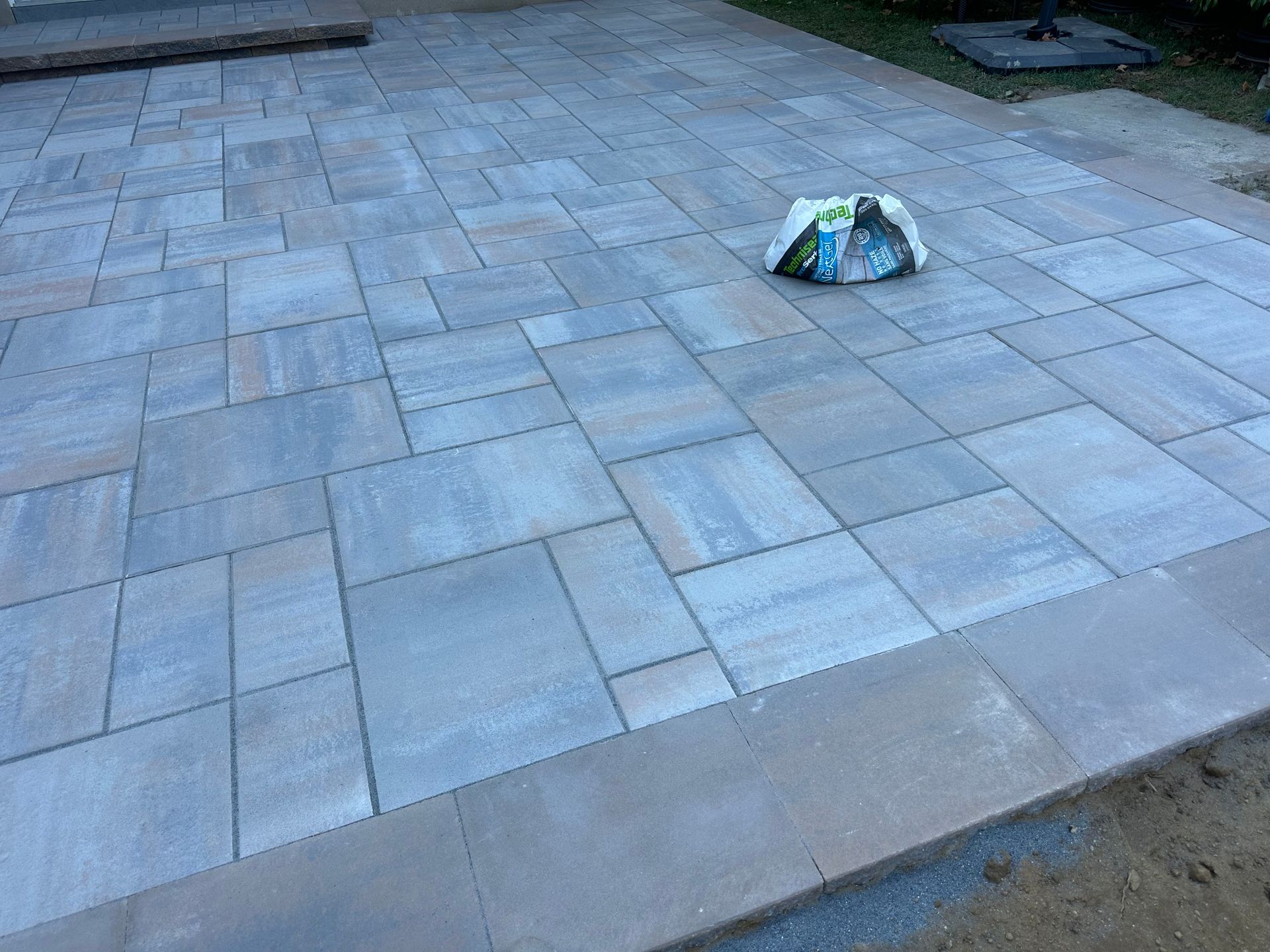 Brick patio with a bag of trash on it. Gray and tan pavers.
