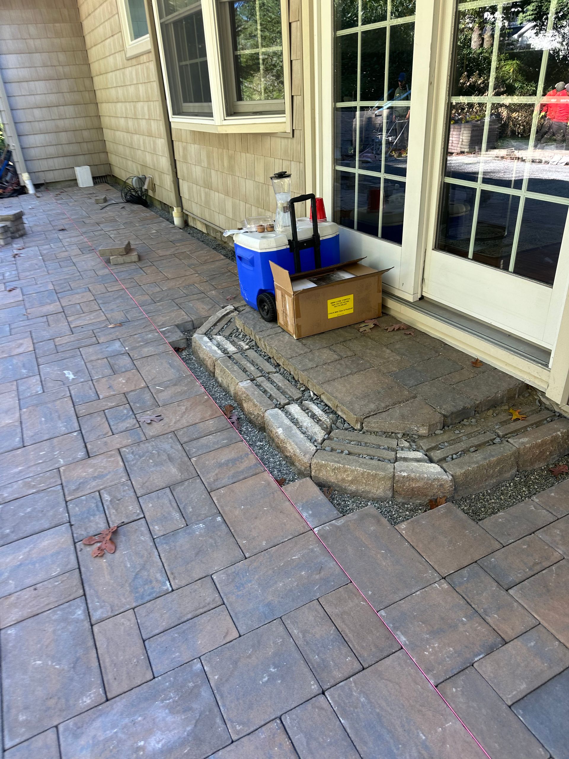 Brick patio with a step leading to a door. A cooler, box, and gravel sit near the door.