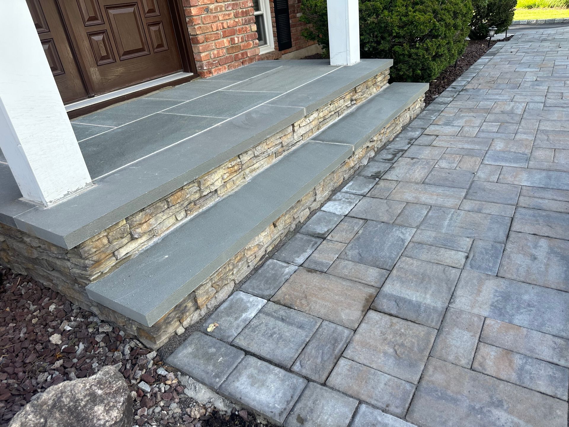 Stone steps with a stone facade lead to a house entrance. A paved walkway is on the right.