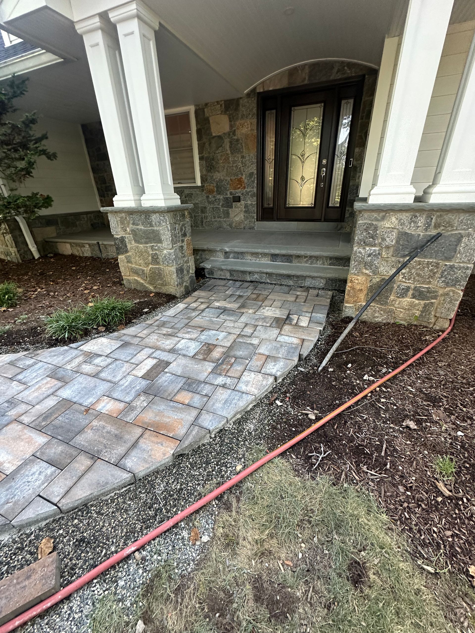 Stone walkway leading to a house entrance with steps and a glass door. Pillars and stone facing.
