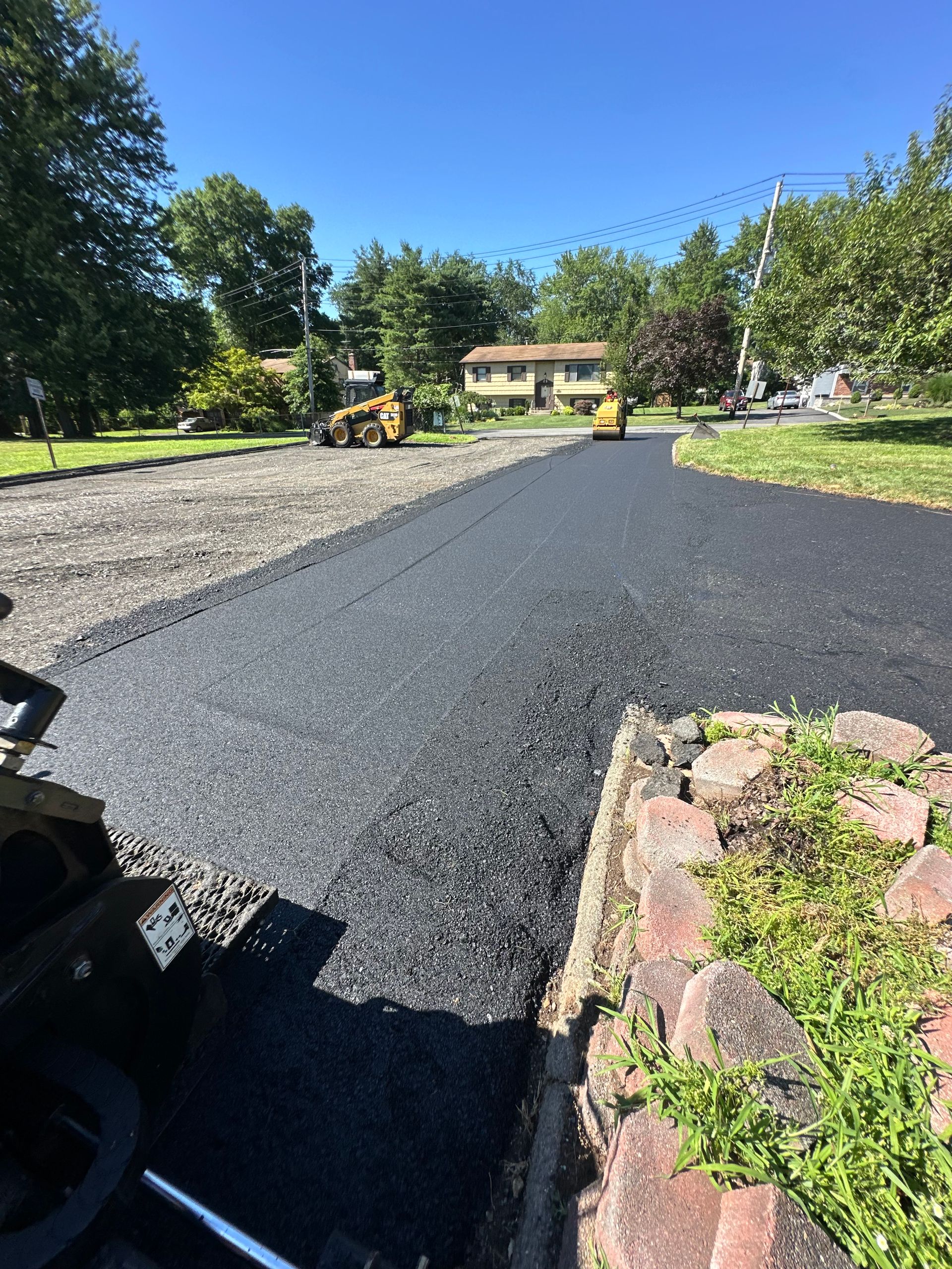 Freshly paved asphalt driveway with construction equipment in the background on a sunny day.