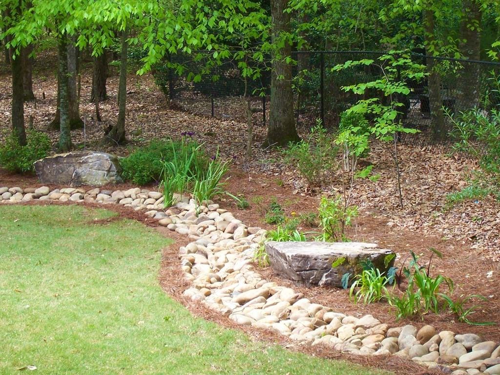 A decorative rock garden with green grass, trees, and two stone structures.