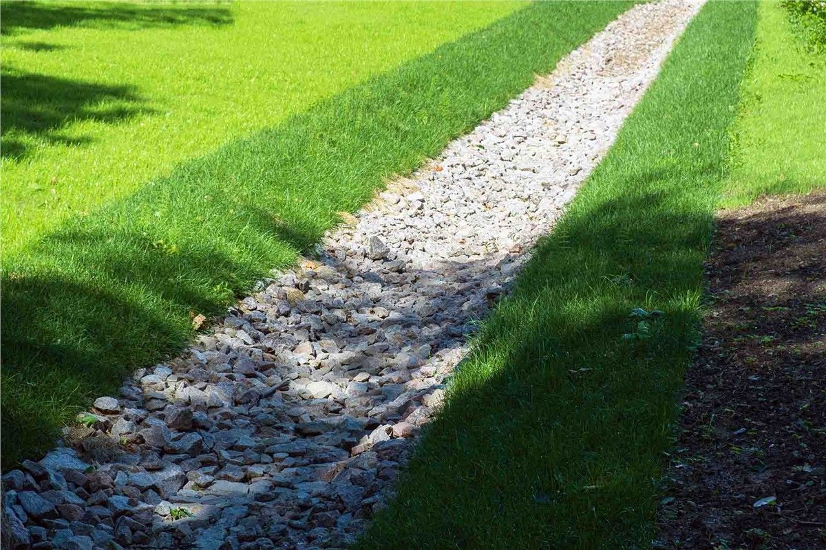 Gravel-lined drainage channel in green lawn.