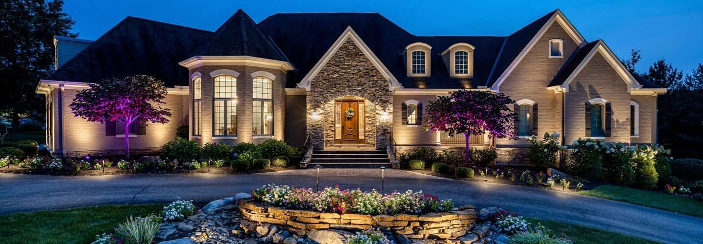 Large, well-lit house at night with stone facade and manicured landscaping.